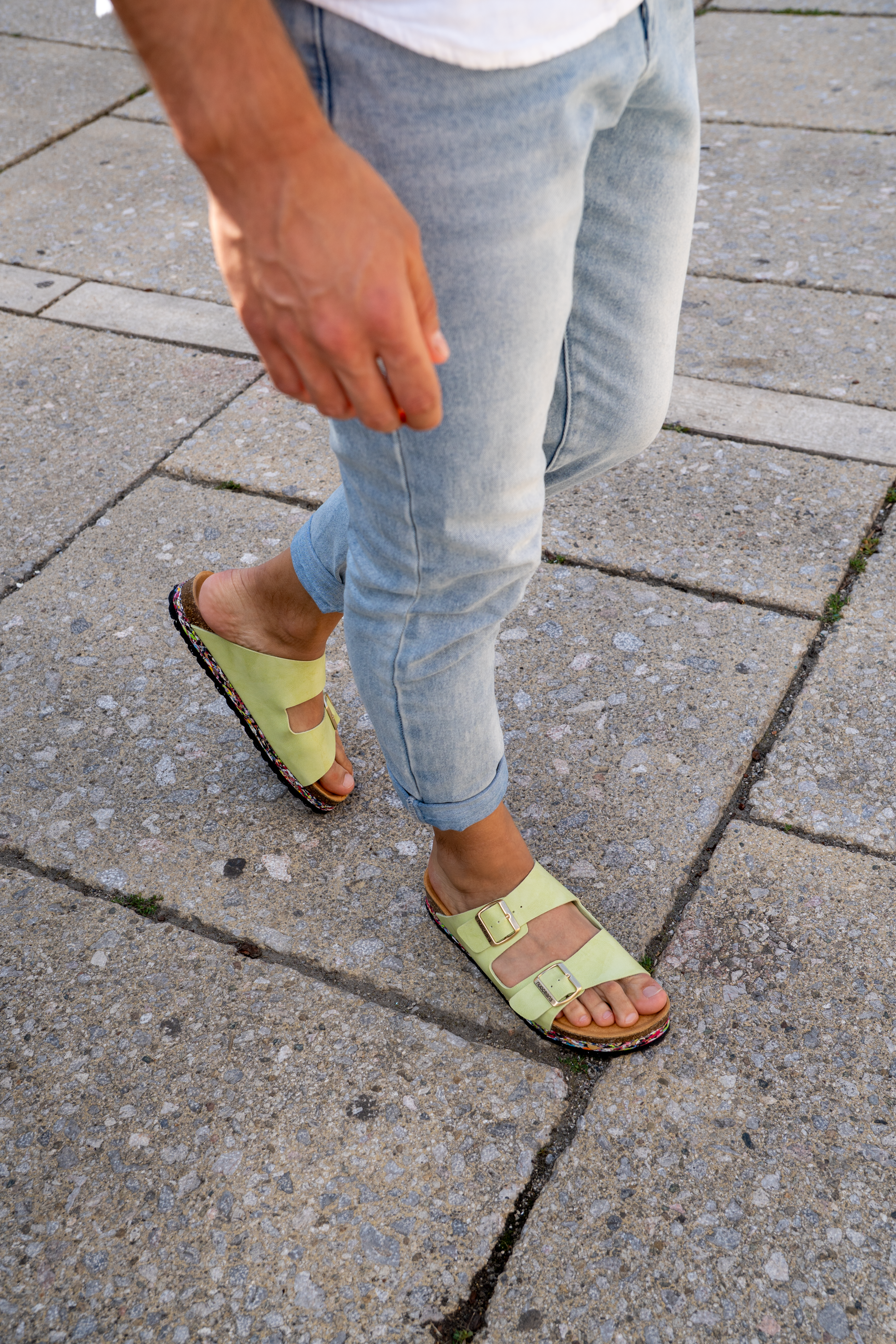 Person wearing light blue jeans and green sandals on a concrete surface